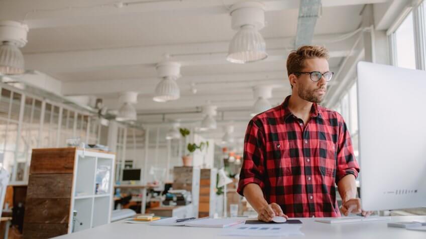 Shot of young businessman in casual clothes at modern startup business office space, working on desktop computer.