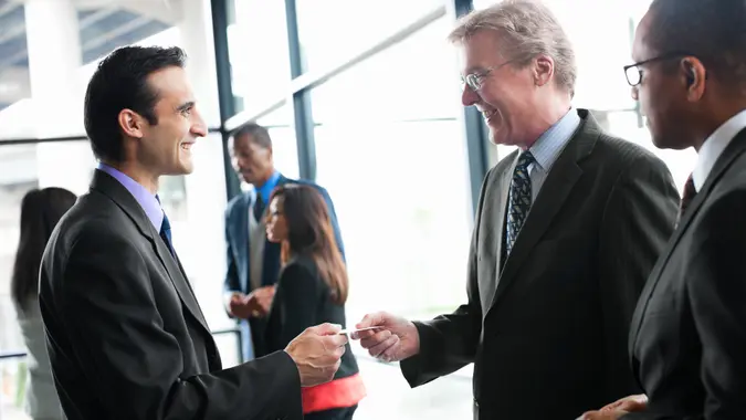 Smiling businessmen exchanging business cards at a networking event in a bright glass office.