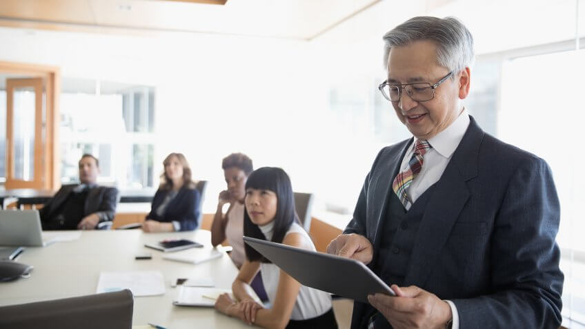Senior businessman with digital tablet leading conference room meeting.