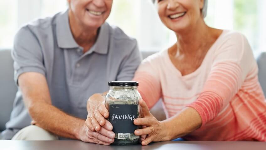 Shot of a senior couple proudly posing with their savings jar.