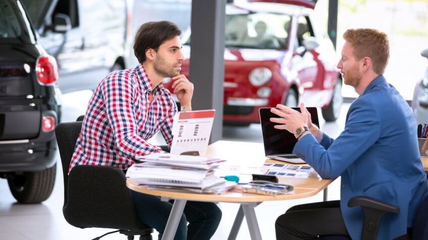 car agent talking with male customer at car dealership saloon.