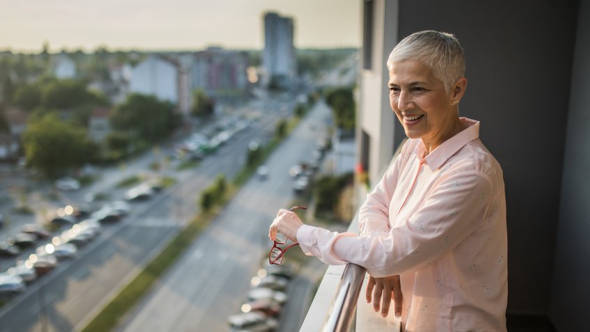 Happy mature woman standing on a penthouse terrace and looking at view.