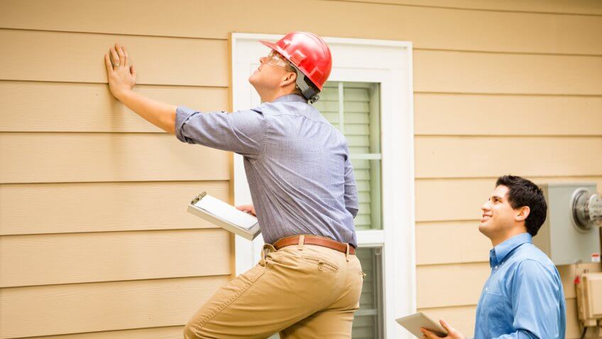 Repairmen, building inspectors, exterminators, engineers, insurance adjusters, or other blue collar workers examine a building/home's exterior wall and foundation.
