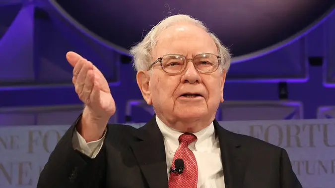 Billionaire Warren Buffett speaking at an event with a purple background.