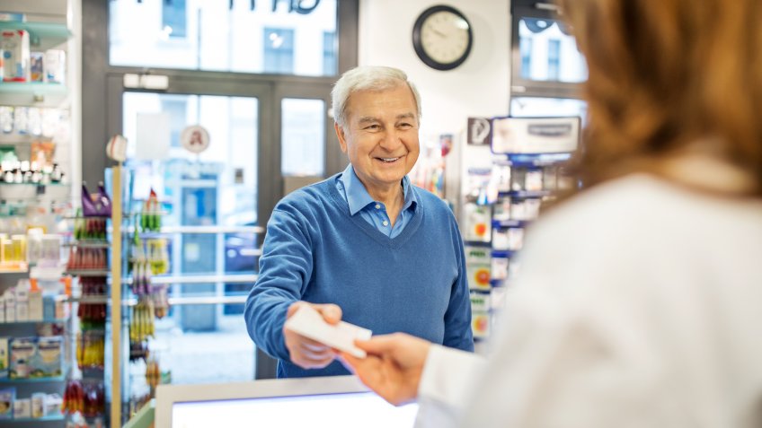 Smiling senior man giving prescription to female pharmacist in store.