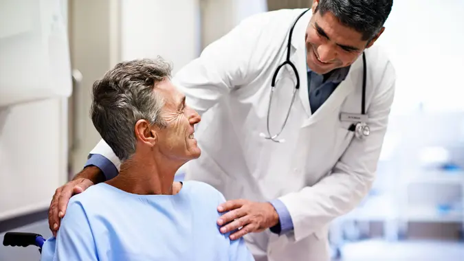 Shot of a doctor talking to a patient in a wheelchair in a hospital corridor.
