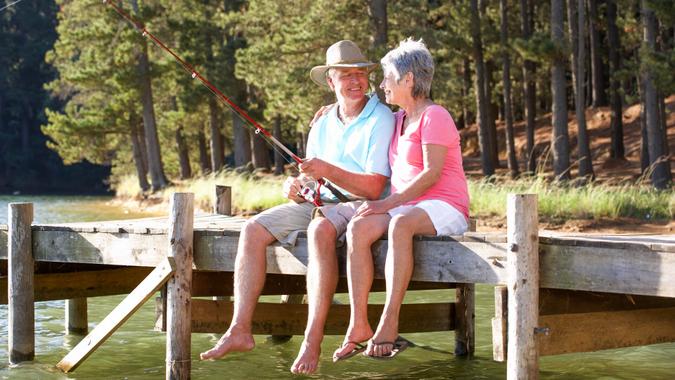 Senior couple sitting on jetty together fishing, enjoying their time in retirement.