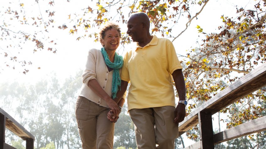 Senior couple walking on footbridge in park.