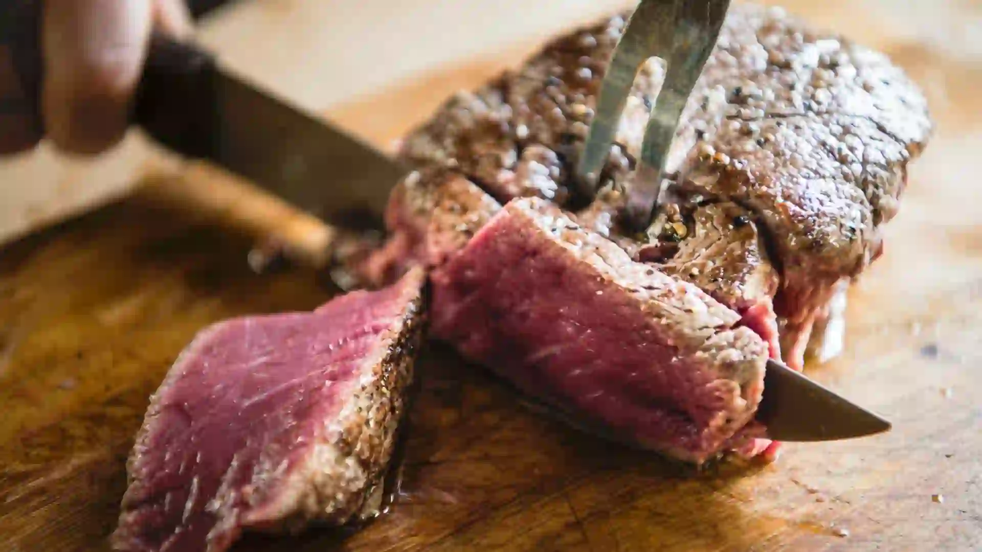 A person cutting into steak and making slices to illustrate beef prices.