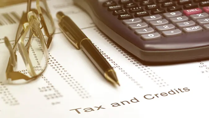 Tax and credits concept image of a pen, calculator and reading glasses on financial documents.