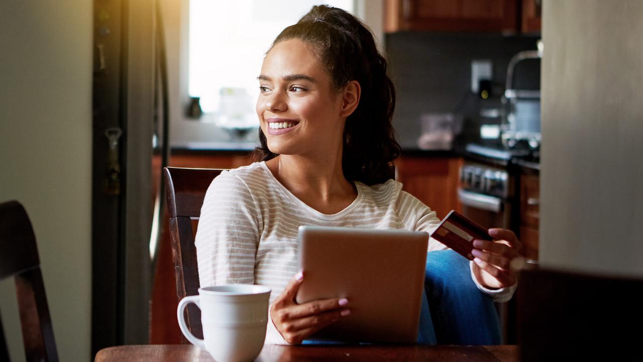 Shot of a young woman drinking coffee and shopping online with her digital tablet at home.