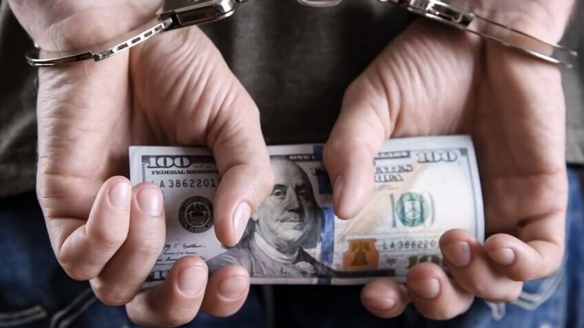 Man in handcuffs holding dollar banknotes behind the back, close up.
