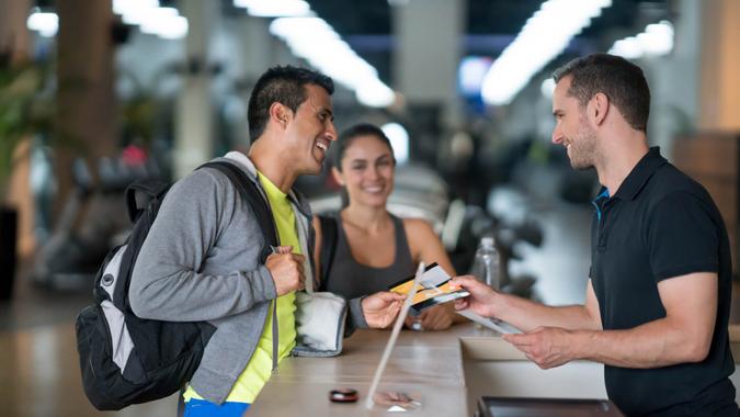 Happy couple of people at the gym talking to the receptionist about membership plans - healthy lifestyle concepts.