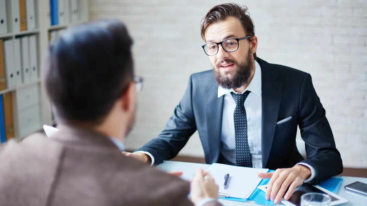 Two men sitting across a desk from each other and having conversation.
