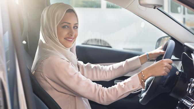 Portrait of a Middle Eastern woman driving a car, she is wearing a modern beige Abaya.