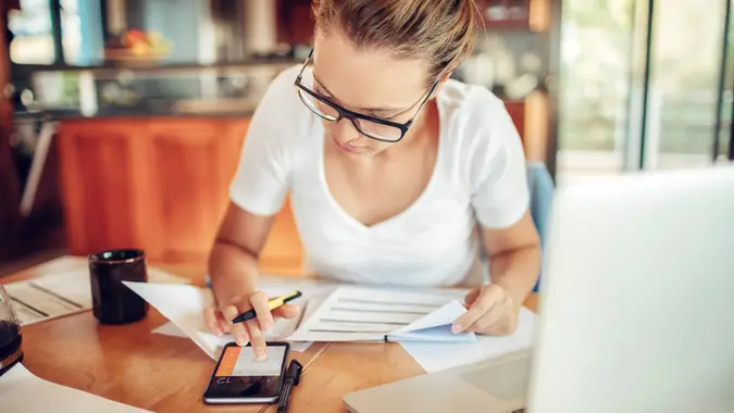 Close up of a young woman sitting in kitchen and  going through her financials.