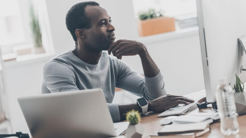 Handsome young African man keeping hand to his face while sitting at his working place in home office.