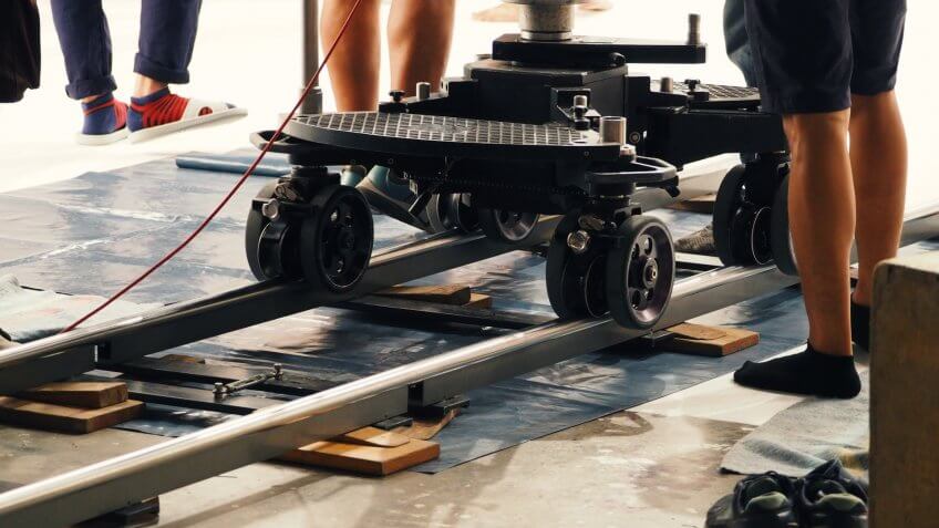 Behind the scenes of production crew team setting dolly track for camera equipment and 4K HD video shooting in a big studio.