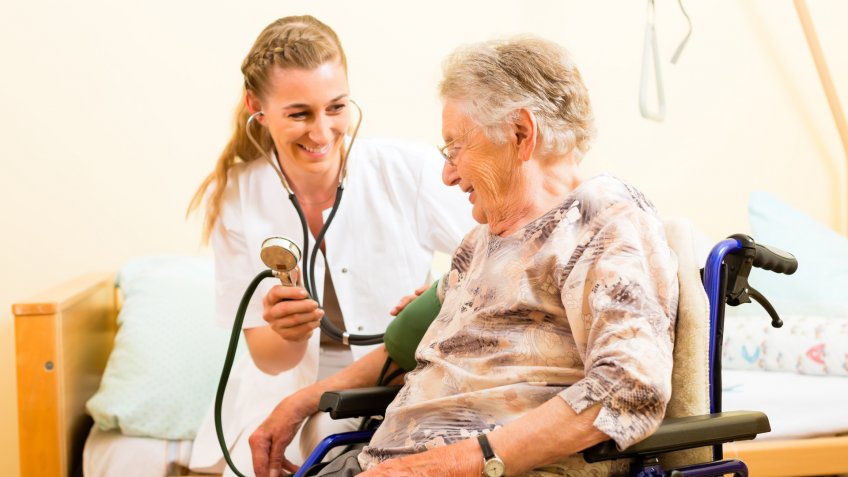Young nurse and female senior in nursing home, the blood pressure is going to be measured.