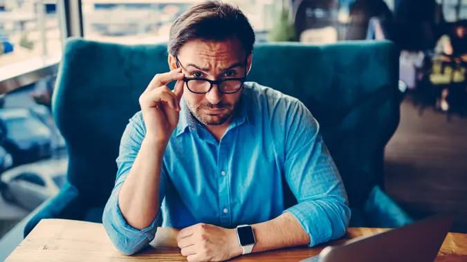 Portrait of handsome proud CEO looking through glasses sceptical doubting in information, confident businessman dislike idea for startup suspiciously getting off spectacles thinking for failure.
