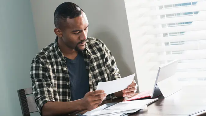 A young African-American man sitting at a table at home, paying bills.