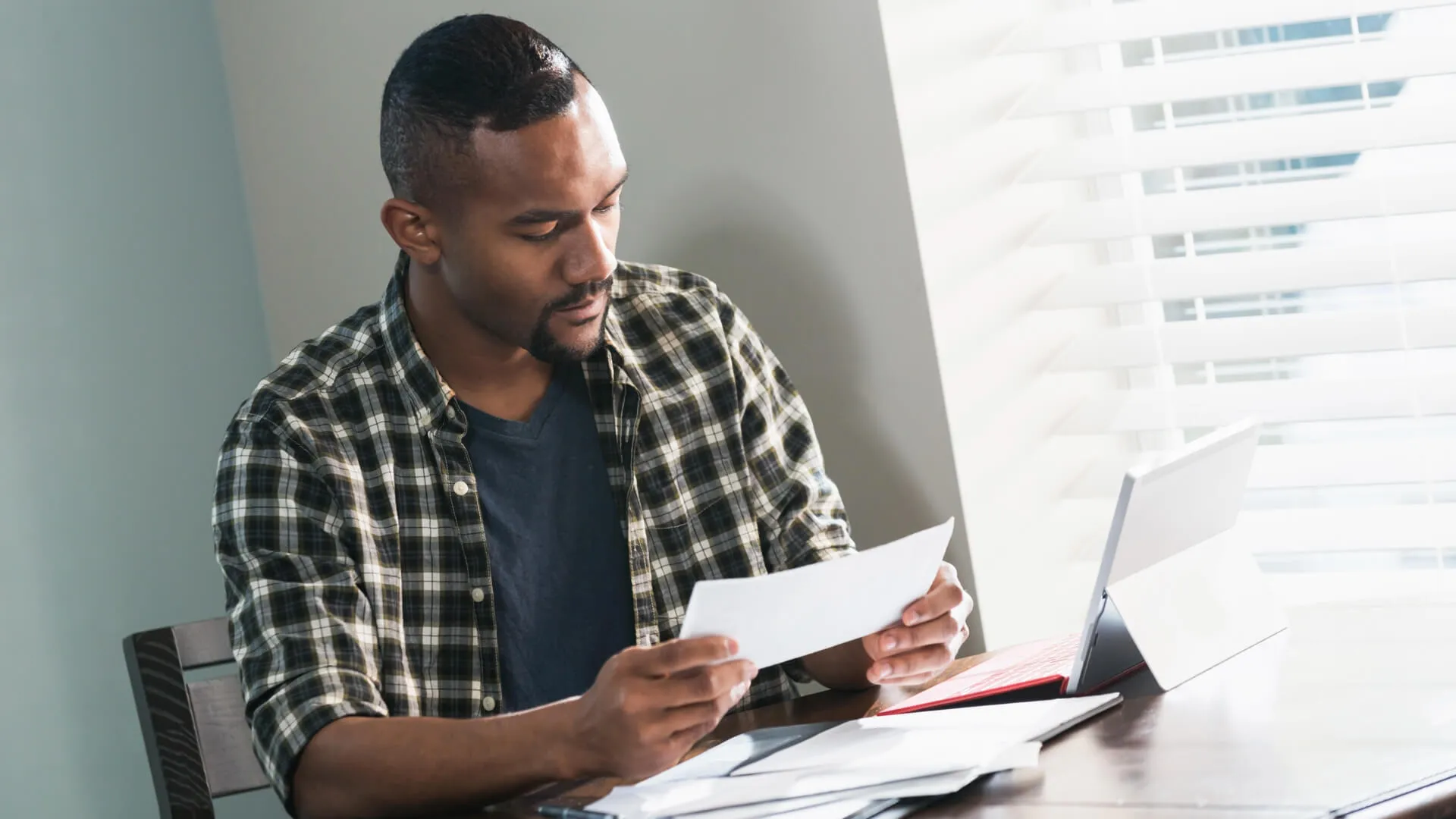 一个年轻的黑人男子坐在一张桌子在家里,付账单。