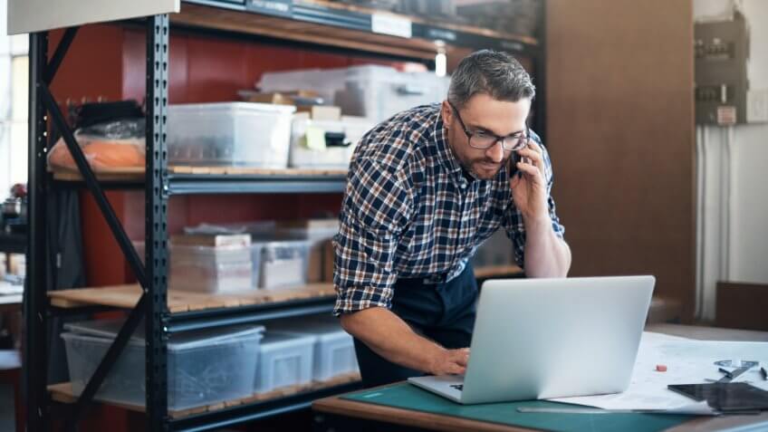 man using a laptop and mobile phone while working on a project in a workshop