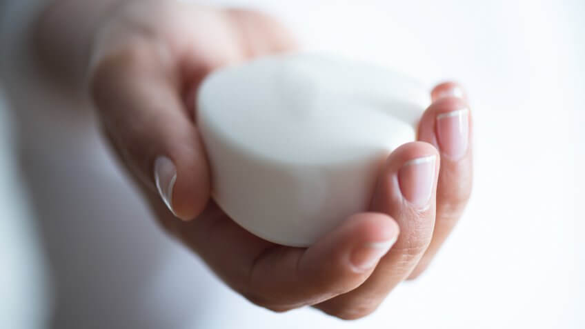 Female hand holds white soap bar in hand, horizontal.