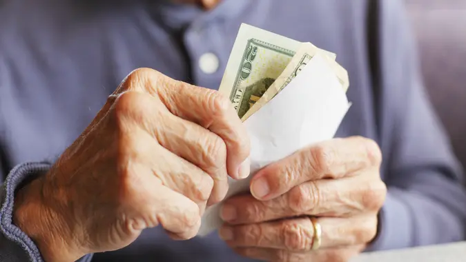 A senior man wearing a gold wedding ring is holding U.