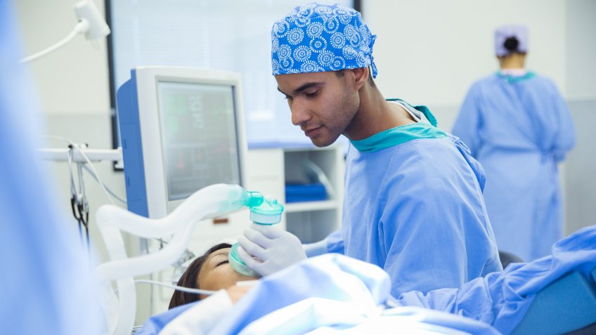 25-29 Years, African Ethnicity, Care, Color Image, Expertise, Face, Head And Shoulders, Holding, Horizontal, Hospital, Indoors, Looking Down, Medical Equipment, Occupation, Operating Table, Patient, Photography, Protection, Safety, Scrubs, Selective Focus, Sitting, Skill, South Africa, Surgical Glove, Two People, Waist Up, Watching, Working, Young Adult, Young Men, anesthesiologist, anesthetic, background people, cape town, healthcare, laying, man, medical, operating gown, operating room, oxygen mask, people, responsibility, surgery, surgical cap