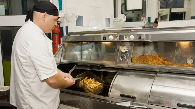 "Interior of a British fish and chip shop, showing a cook removing chips from the fryer.