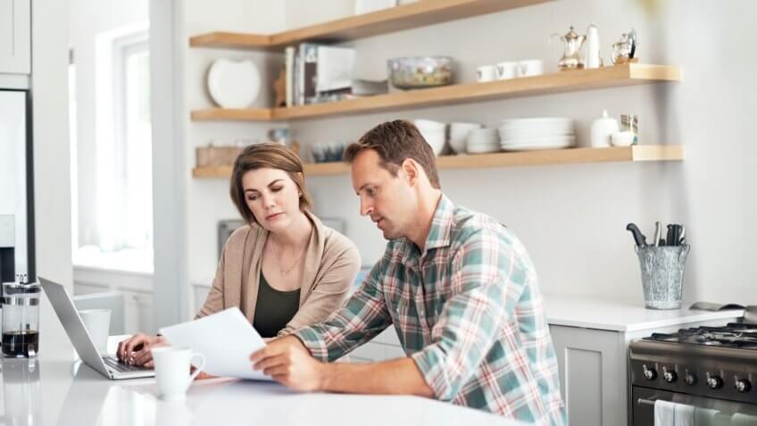 Shot of a couple using a laptop while going through paperwork together at home.