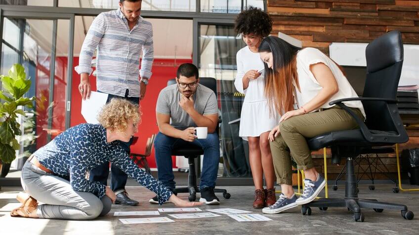 Creative people looking at project plan laid out on floor.