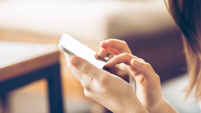 Young happy woman typing on smart phone.