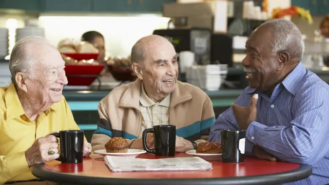 a group of three older men sitting and talking and drinking coffee