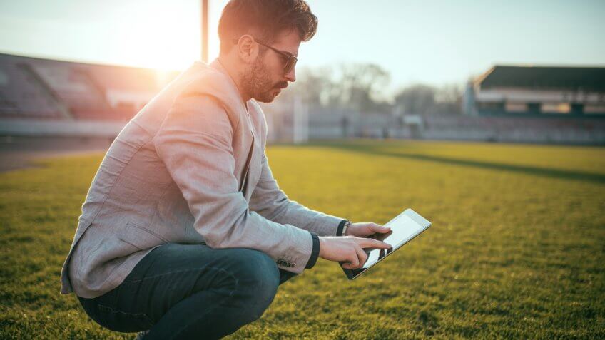 Young and successful footbal manager holding a digital tablet out on the football field.