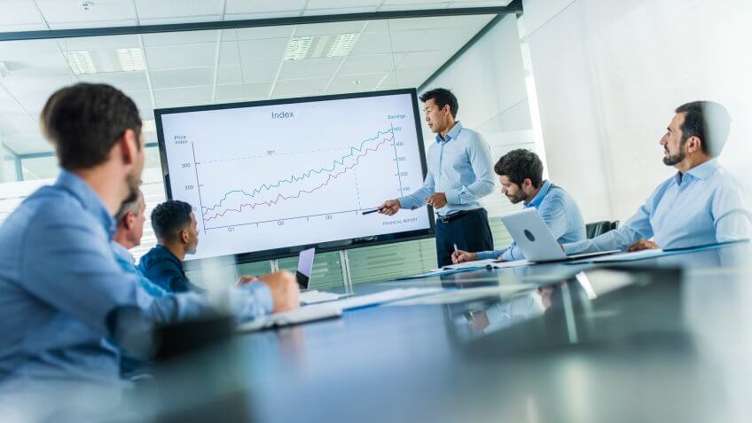 Man of asian ethnicity talking to a group of businessmen and explaining an investment opportunity chart.