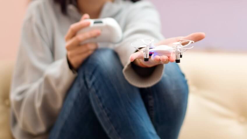 Close-up of woman's hands with a remote control and small drone at home.