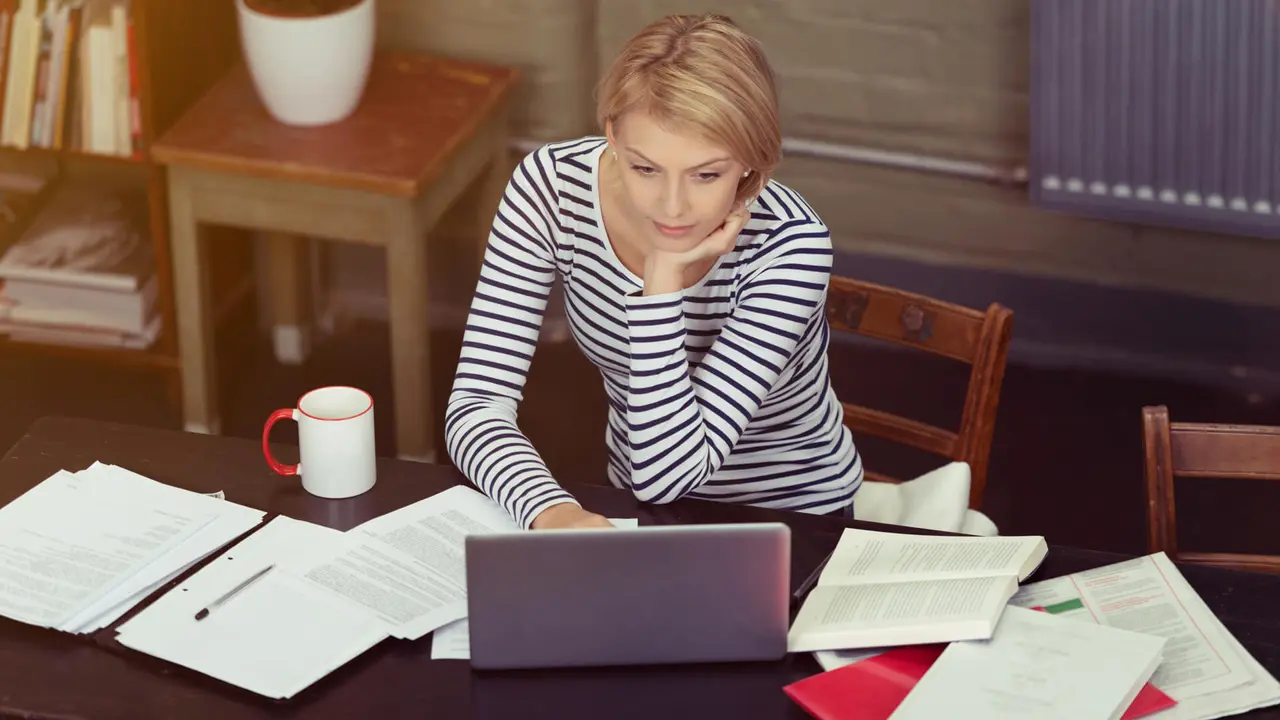 Attractive businesswoman surrounded by paperwork as she sits at her desk working on a laptop computer, high angle view.