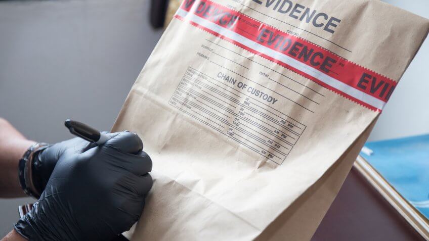 forensic 's hand in black glove writing on evidence bag and seal by red tape in crime scene investigation.