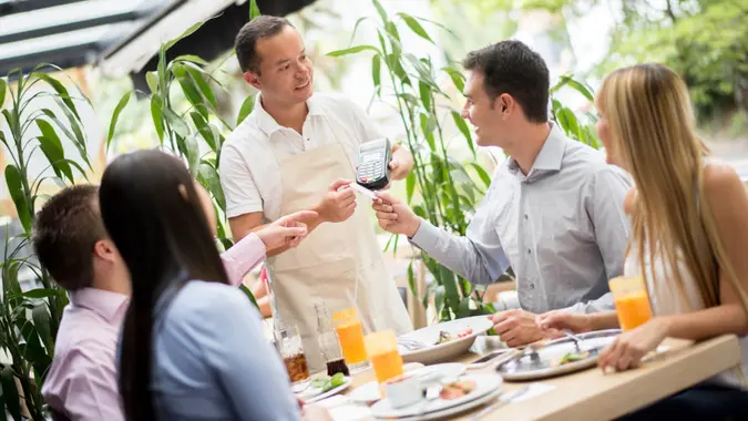 Man paying by credit card at a restaurant while having dinner with friends.