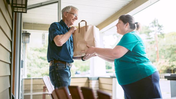 A kind and caring neighbor or friend delivers fresh produce from the grocery store to an elderly man at his home.