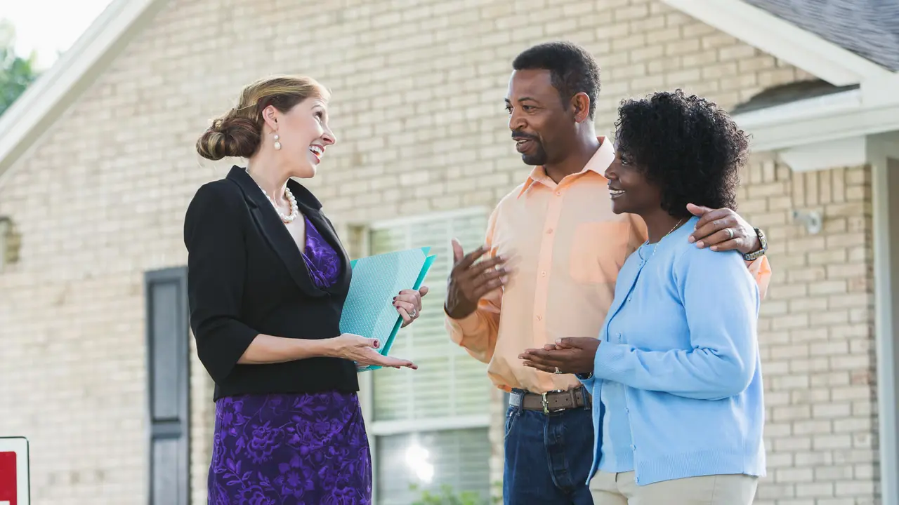 A female real estate agent standing outside a house with a couple interested in buying