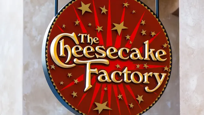 The Cheesecake Factory logo sign hanging outside a restaurant.