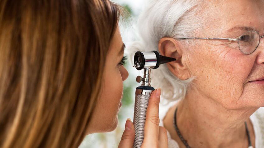 Doctor holding otoscope and examining ear of senior woman in ambulance.