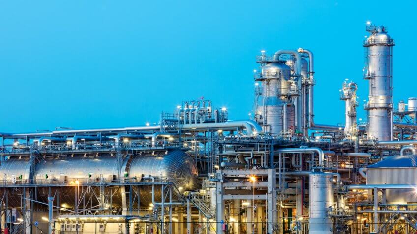 A modern, illuminated refinery is visible at dusk.