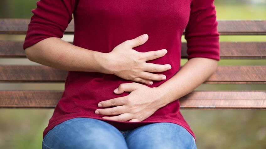 Woman Has Stomach Ache Sitting on Bench at Park.