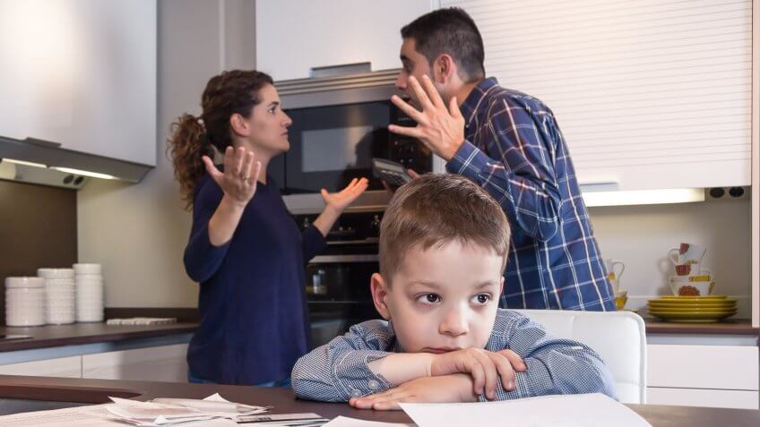Sad child suffering and his parents having hard discussion in a home kitchen by couple difficulties.
