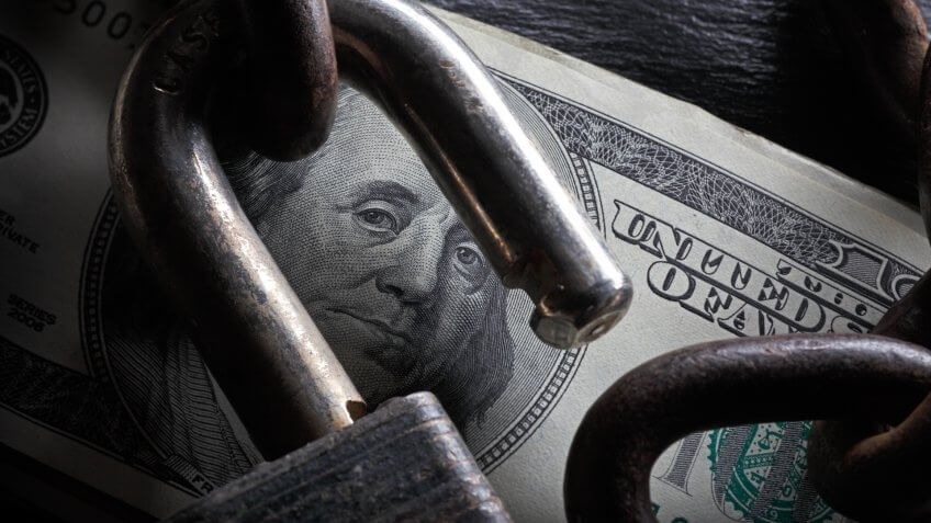 An open lock on a stack of $100 bills.