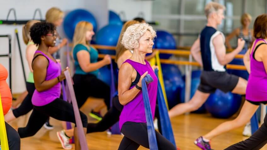A multi-aged and multi-ethnic group of adults using elastic bands to help their strength training workout in a fitness class at a community complex.